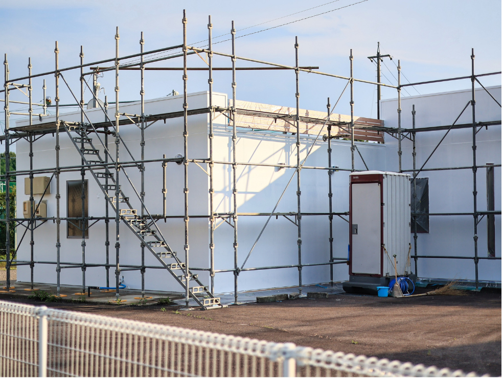 Acabado de exteriores en naves industriales y obra civil. Fachada exterior de una edificación con andamios instalados para la aplicación de pintura industrial y servicios de acabado de interiores y exteriores en naves industriales como parte de trabajos de obra civil.