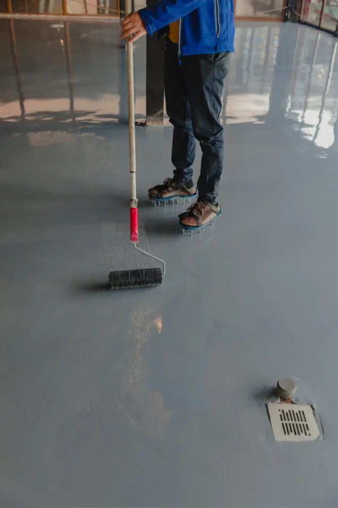 Especialista utilizando rodillo de picos y zapatos de clavos en la aplicación de pisos epóxicos autonivelantes en pisos industriales.